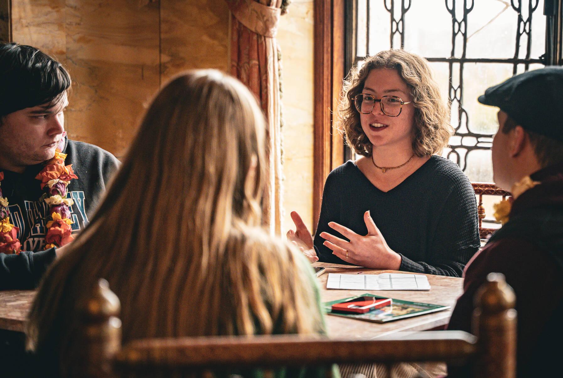 Four students sitting at a table, one of whom is talking and gesturing while the others listen.